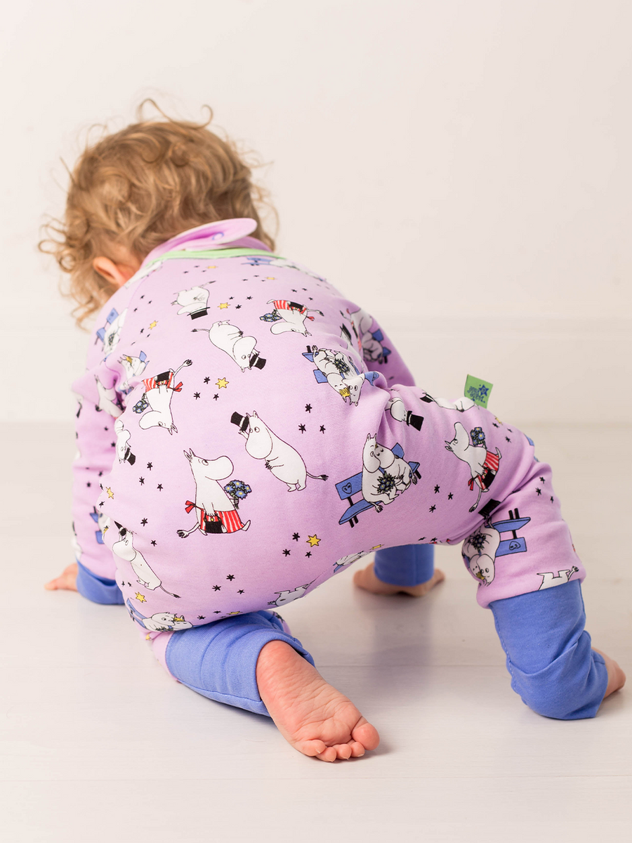 Child wearing a purple romper with moomin cartoon characters on a plain background