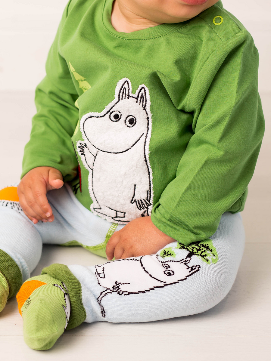 Child wearing a green shirt and blue leggings with Moomin cartoon character designs on a plain background