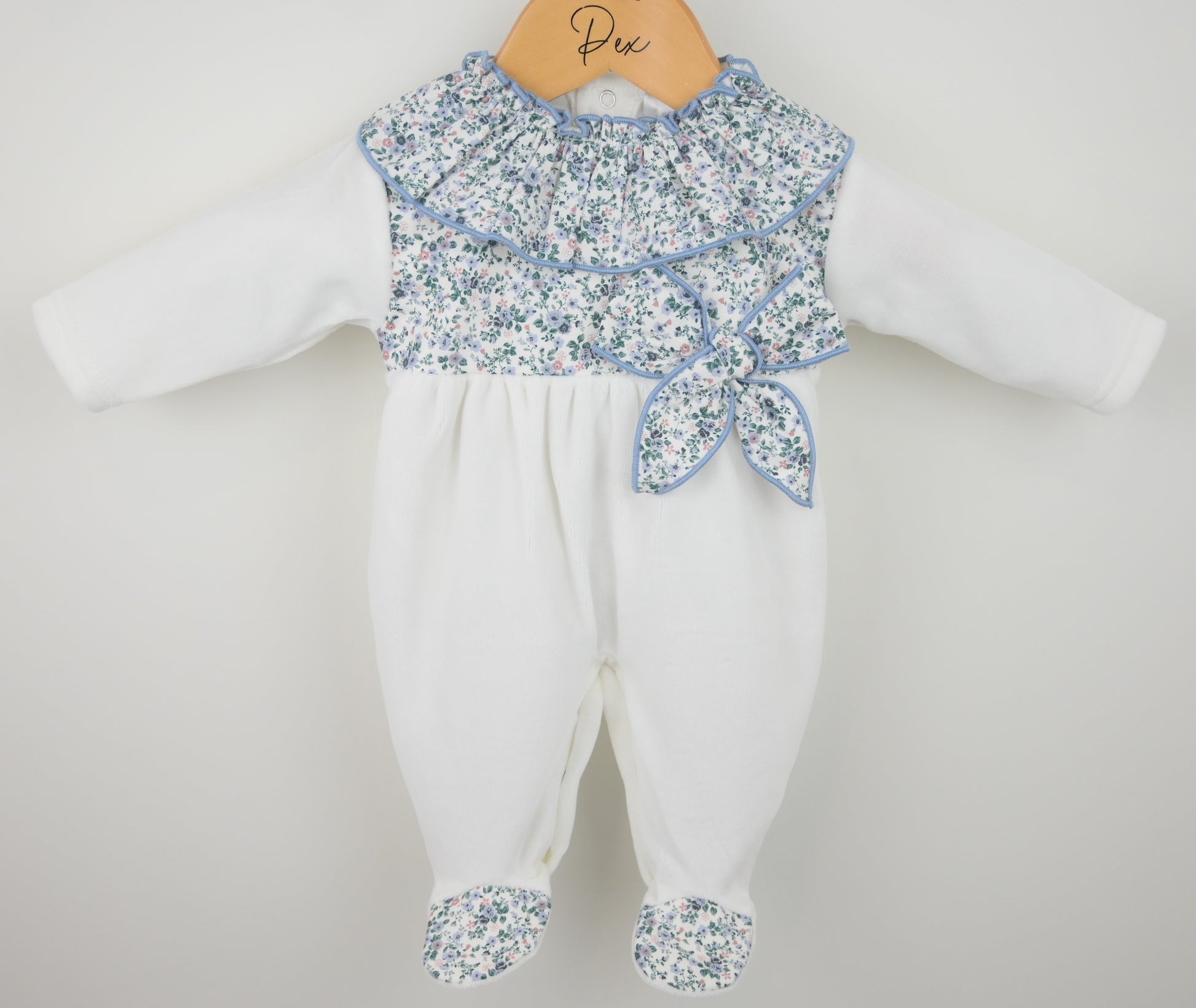 Baby romper with floral top and white pants on a hanger against a light gray background