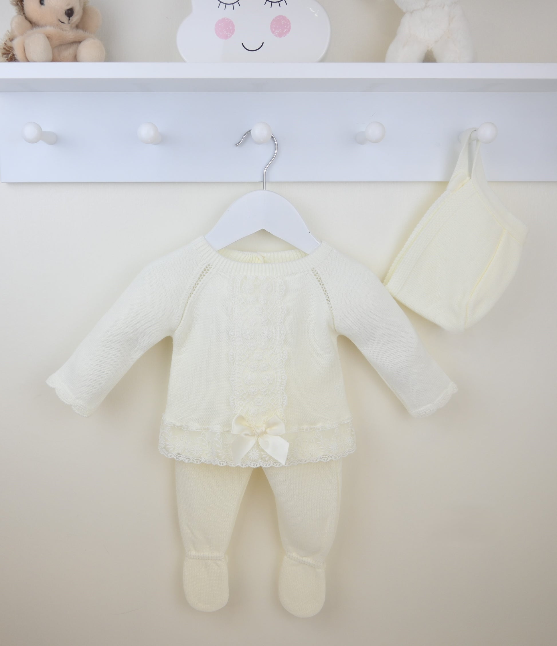 Baby outfit with ivory top and pants hanging on a white shelf.