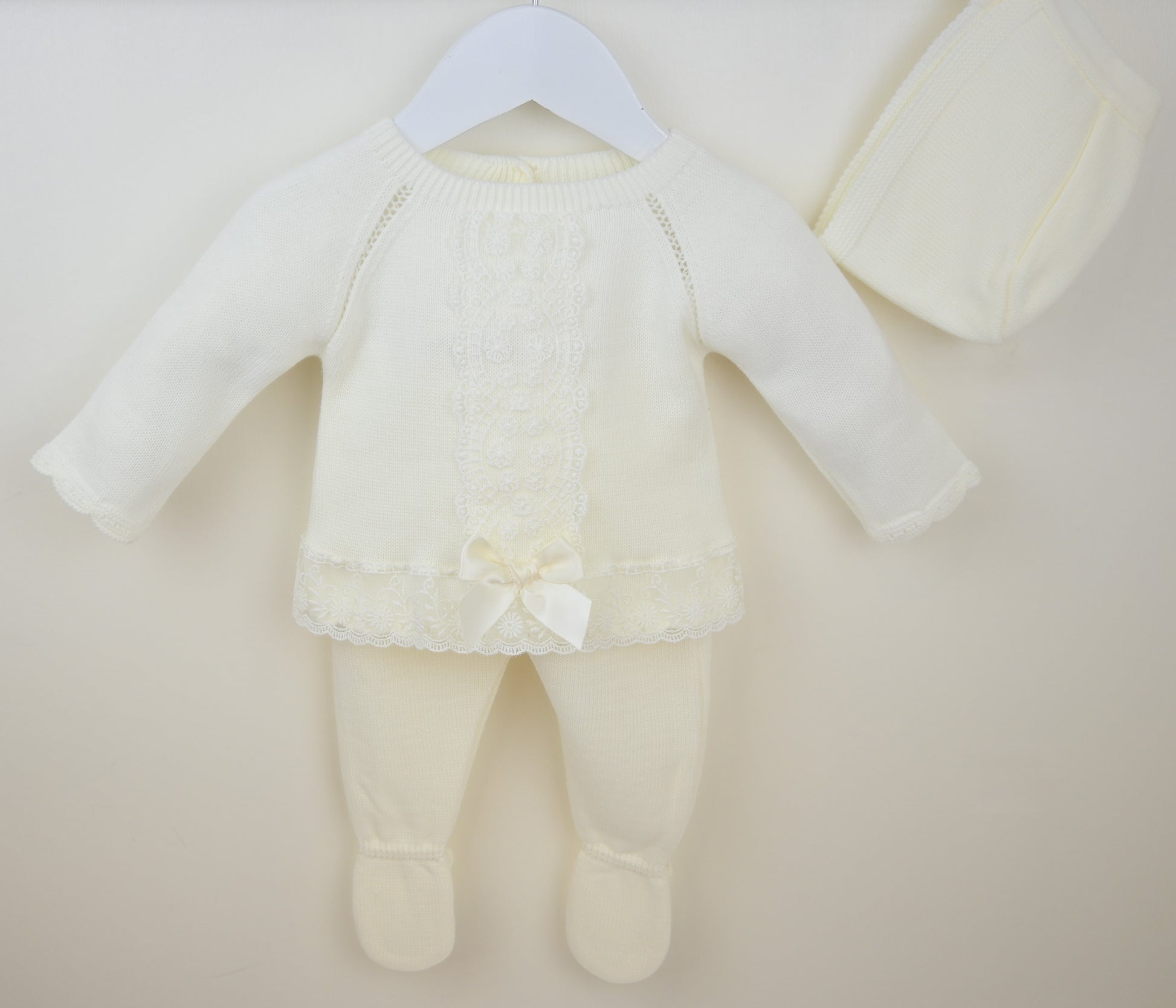 Ivory baby outfit with a bow on a beige background
