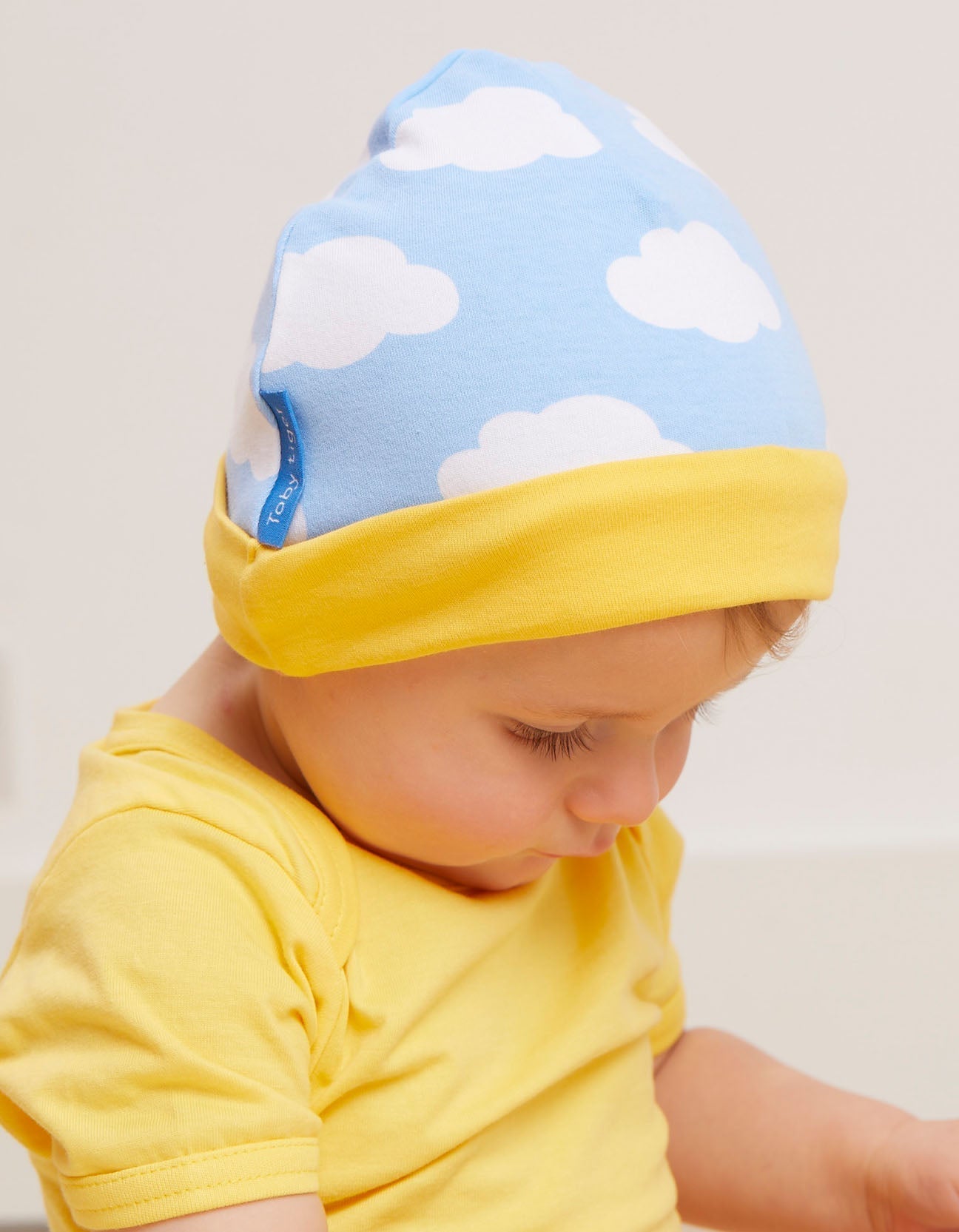 Baby wearing a blue and yellow hat with cloud pattern on a plain background.