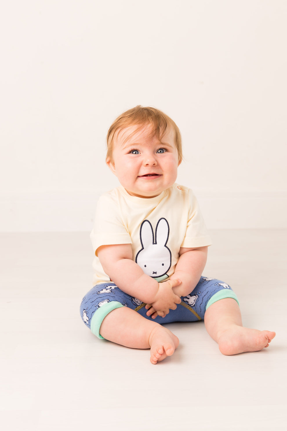 Baby wearing a tshirt with a miffy cartoon character on a white background