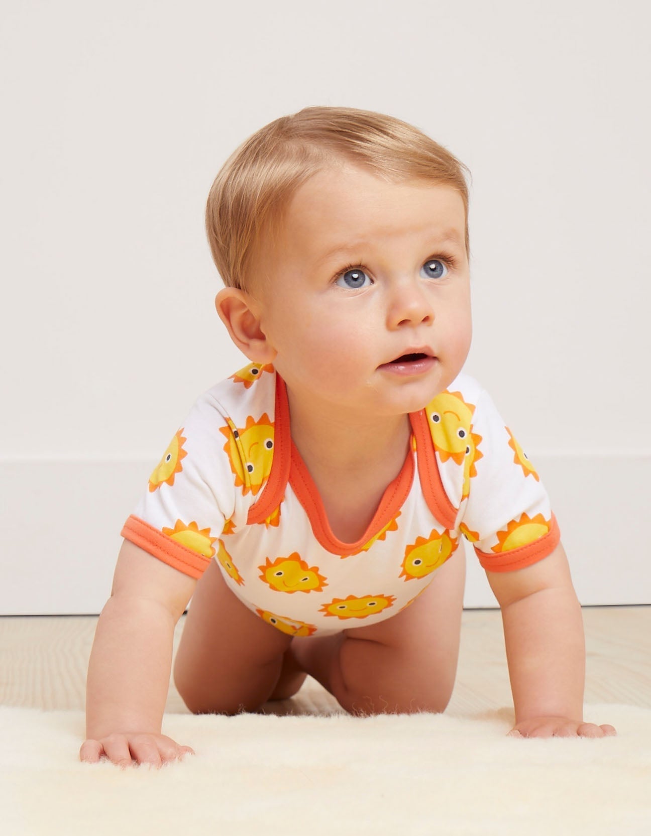 Baby wearing a white vest with orange trim and yellow smiling sun patterns on a light background.