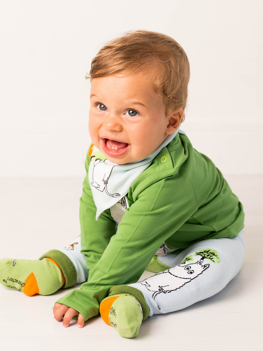 Baby wearing green and blue outfit with Moomin designs on a white background