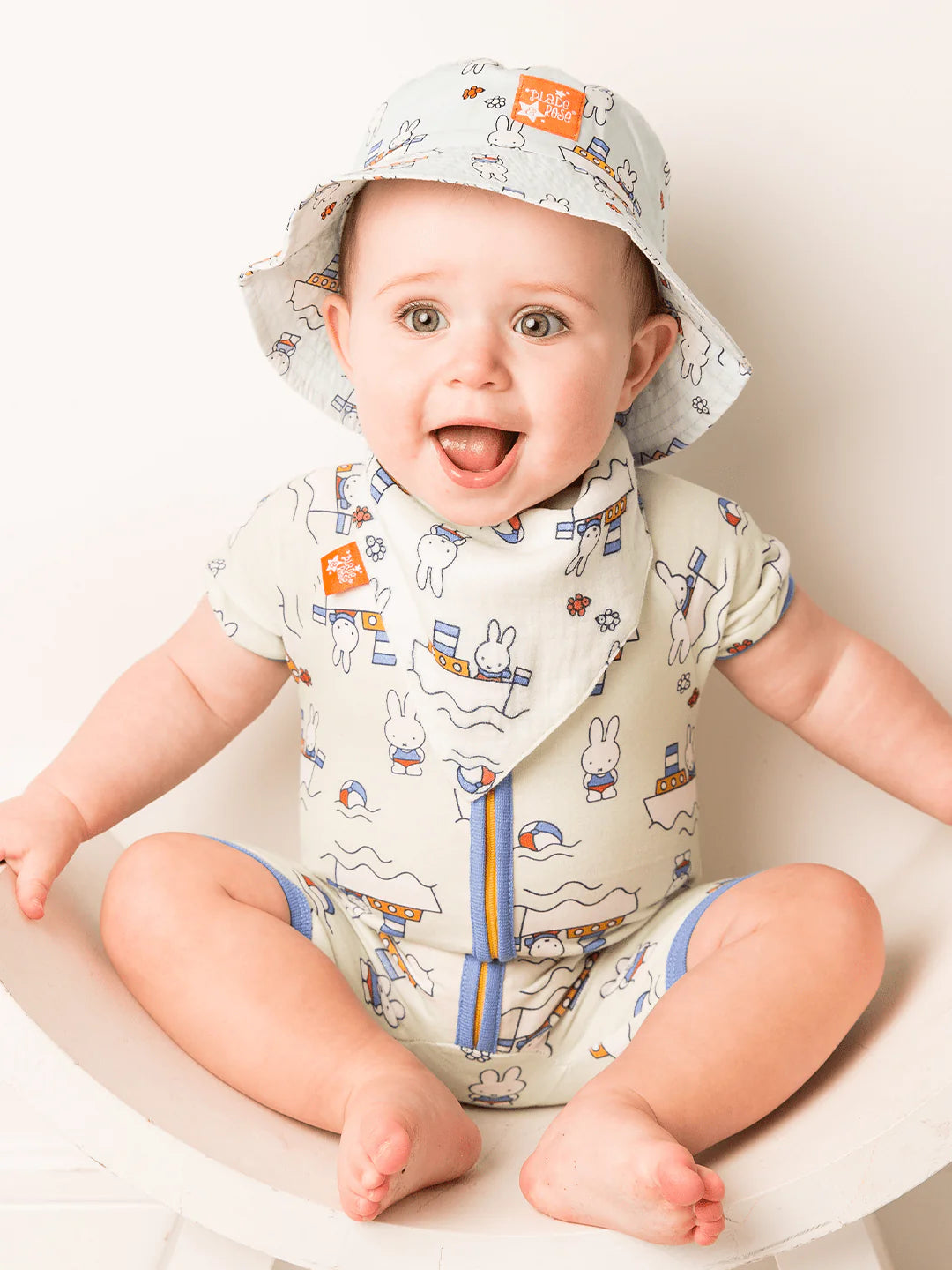 Baby wearing a Miffy patterned romper and hat sitting on a chair.