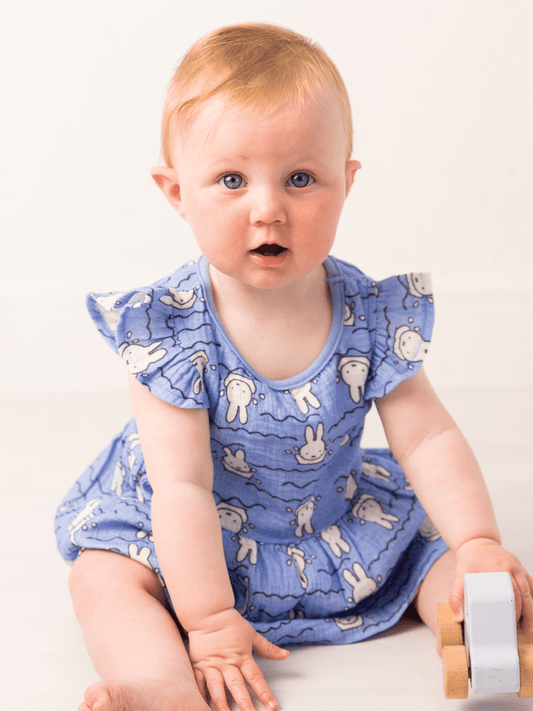 Baby wearing a blue dress with Miffy cartoon patterns on a white background