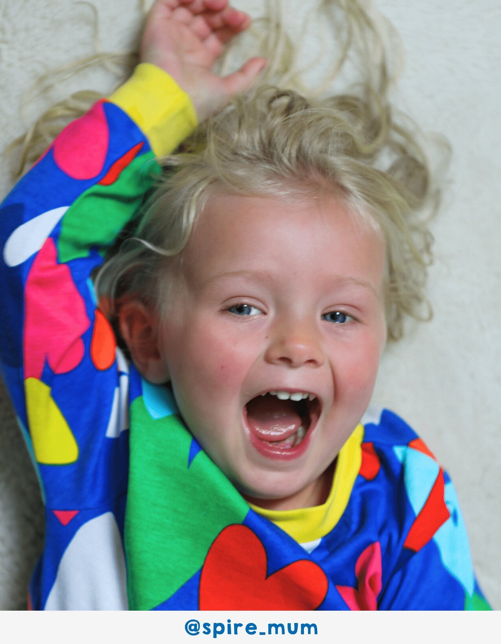 Child wearing colourful pyjama set with hearts, lying on a light-coloured surface.
