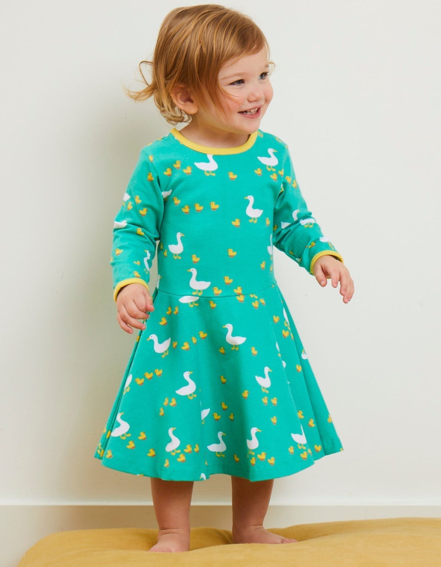 Child wearing a green dress with duck pattern on a plain background