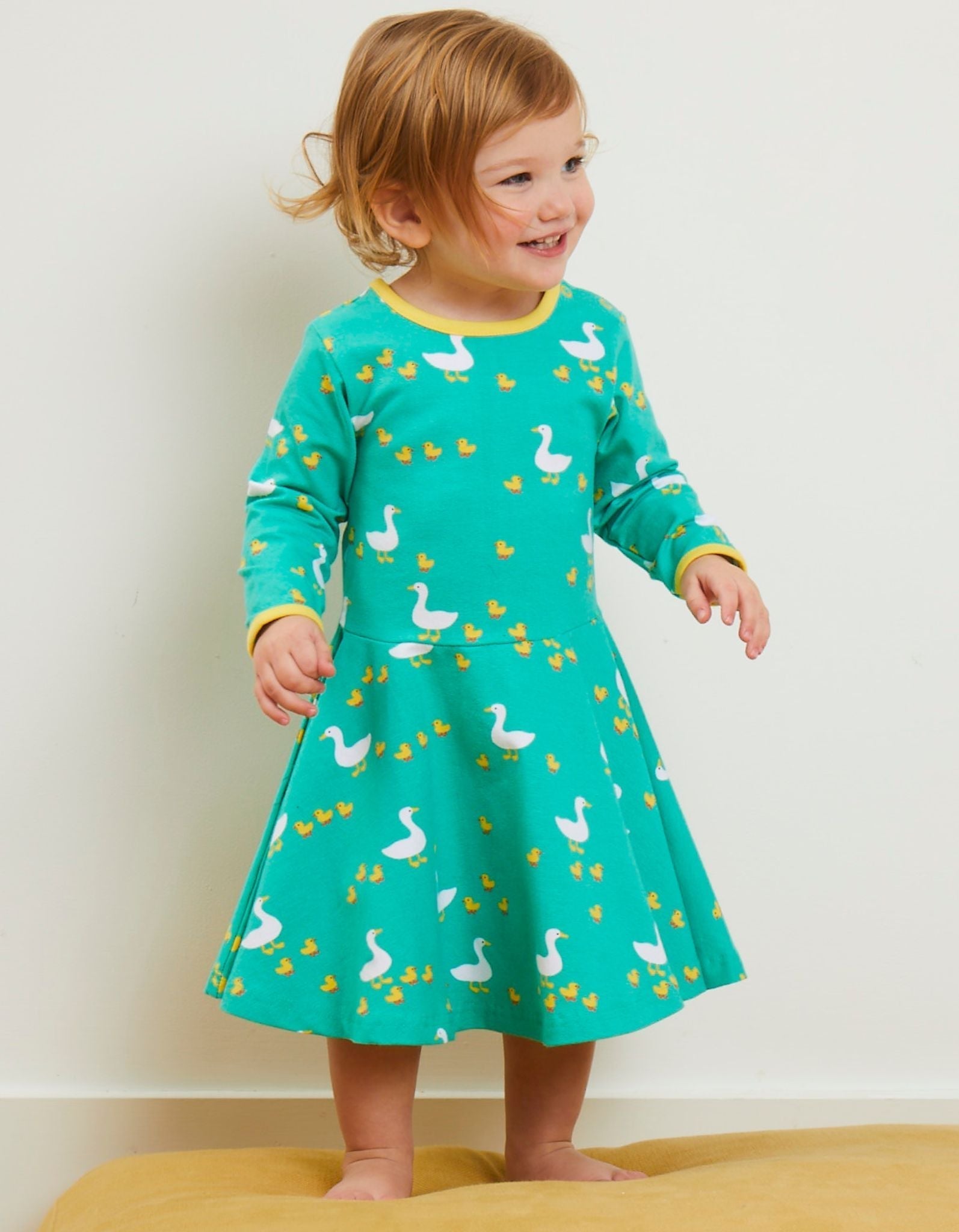 Child wearing a green dress with duck pattern on a plain background