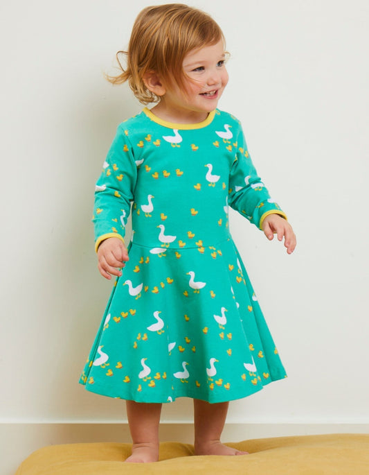 Child wearing a green dress with duck pattern on a plain background