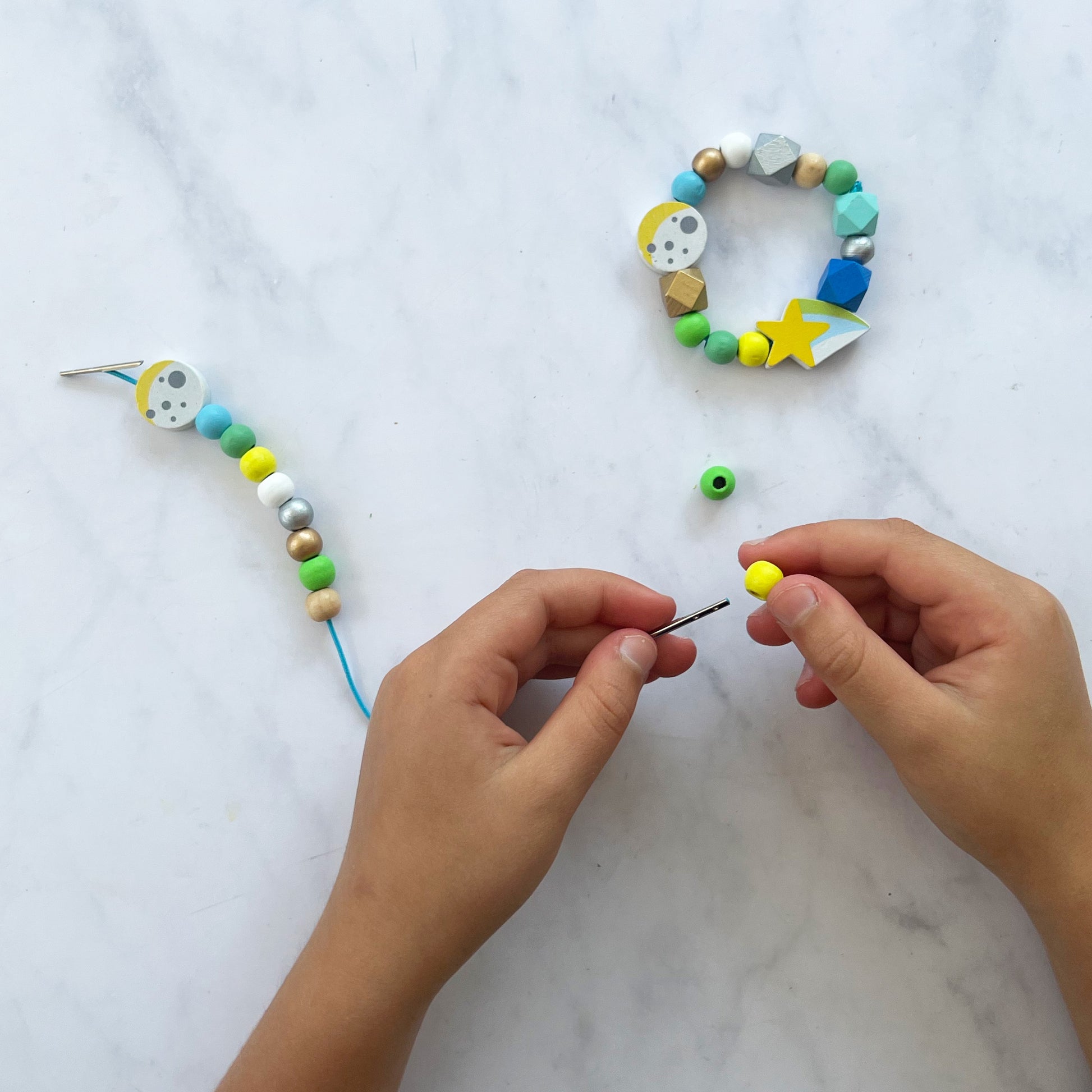 Hands working on a beaded necklace with colorful beads on a marble surface