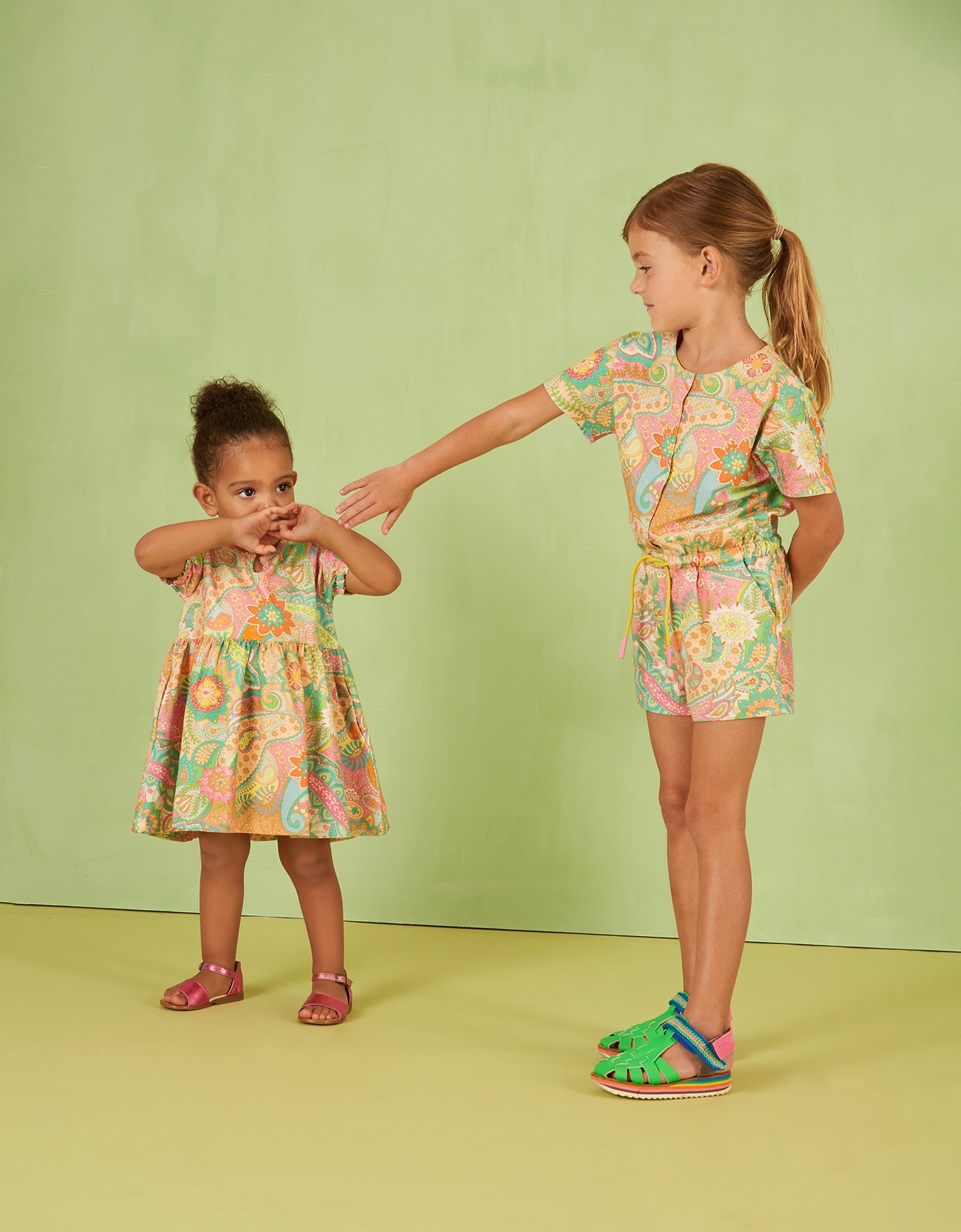 Two children wearing matching floral Oilily paisley outfits on a green background