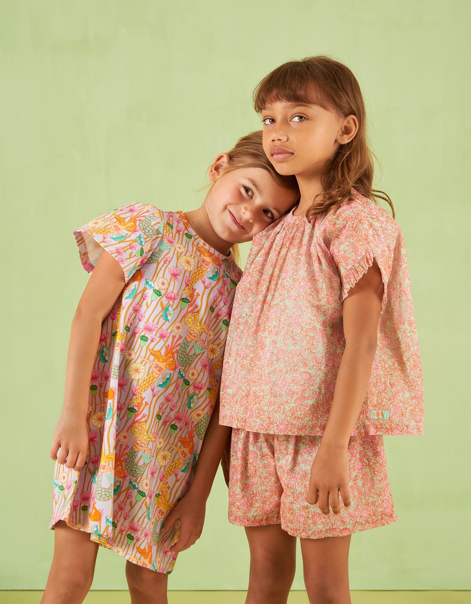Two young girls wearing colorful Oilily outfits against a light green background