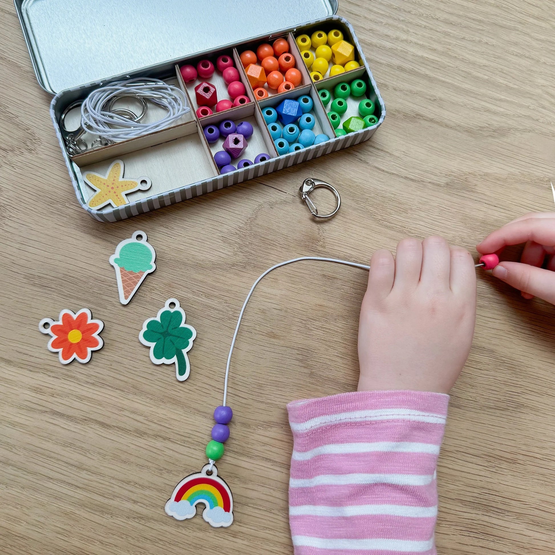 Child's hand working with colorful beads and charm on a wooden table