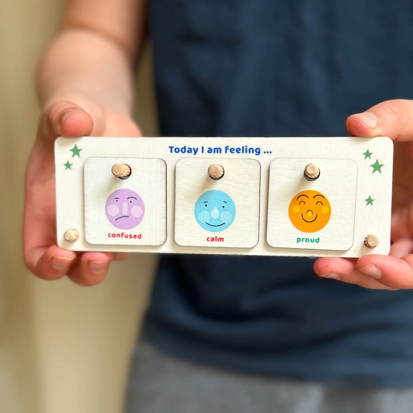 Person holding a feelings board with three emotion cards labeled 'confused', 'calm', and 'proud'.