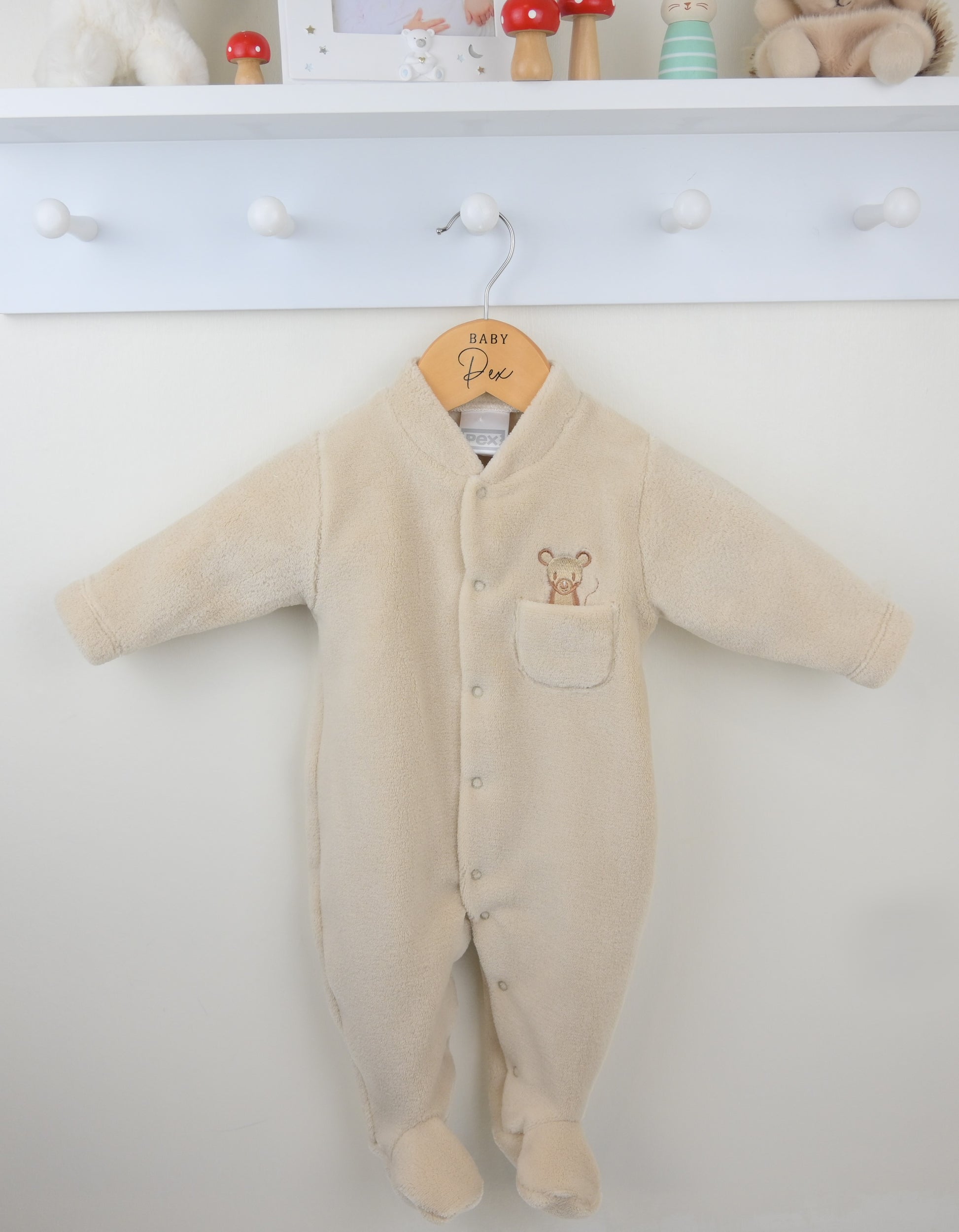 Beige baby onesie with a mouse design on a white wall