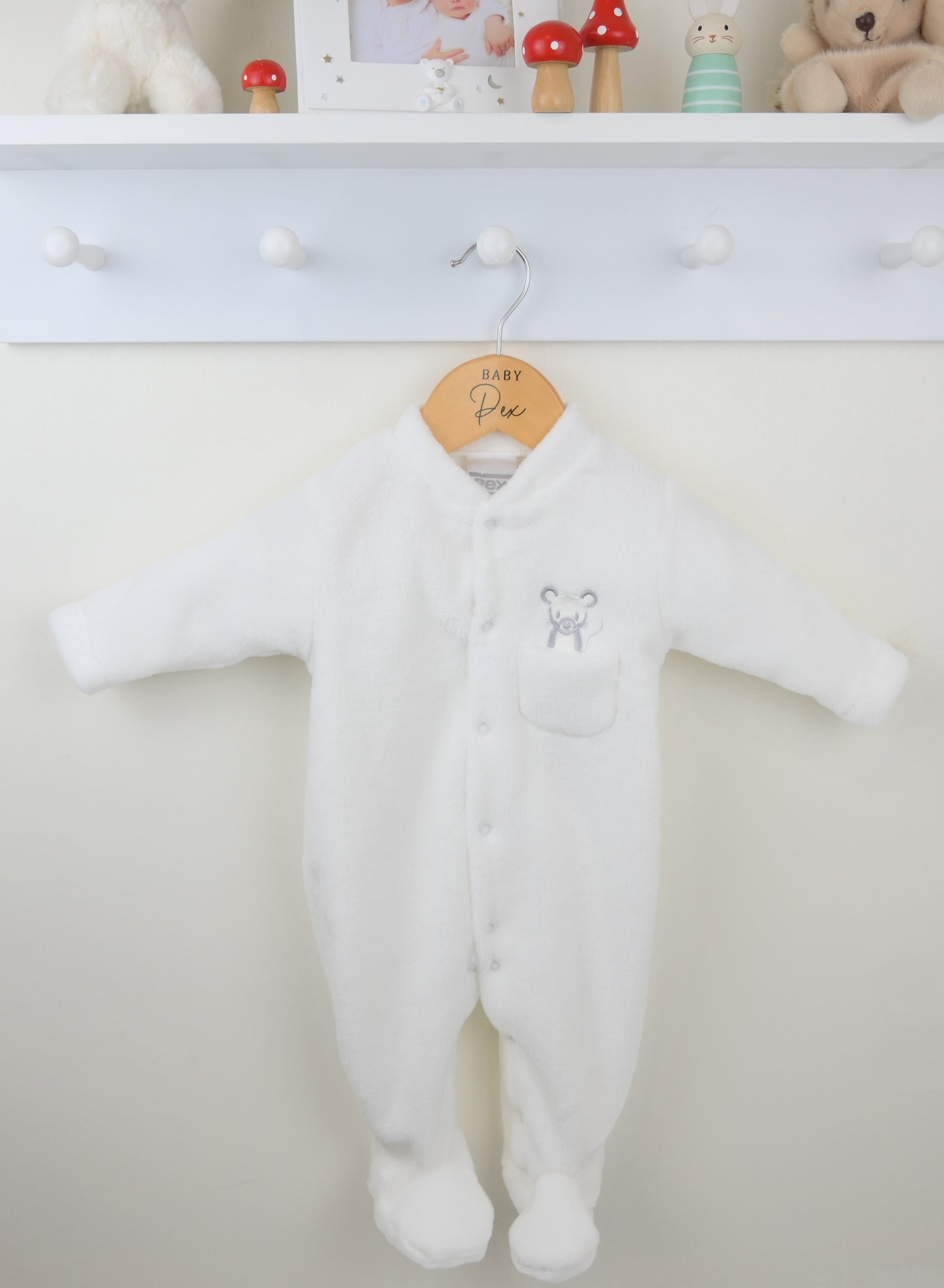White baby onesie hanging on a hook with a neutral background