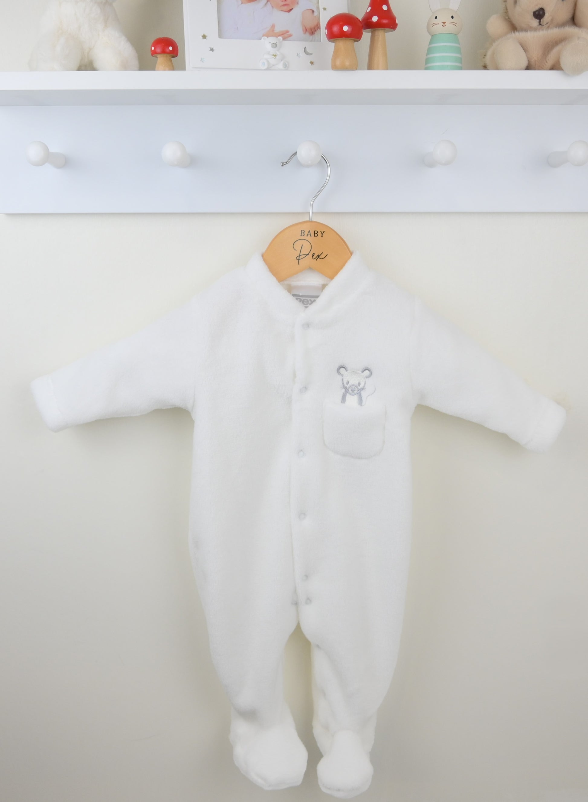 White baby onesie hanging on a hook with a neutral background