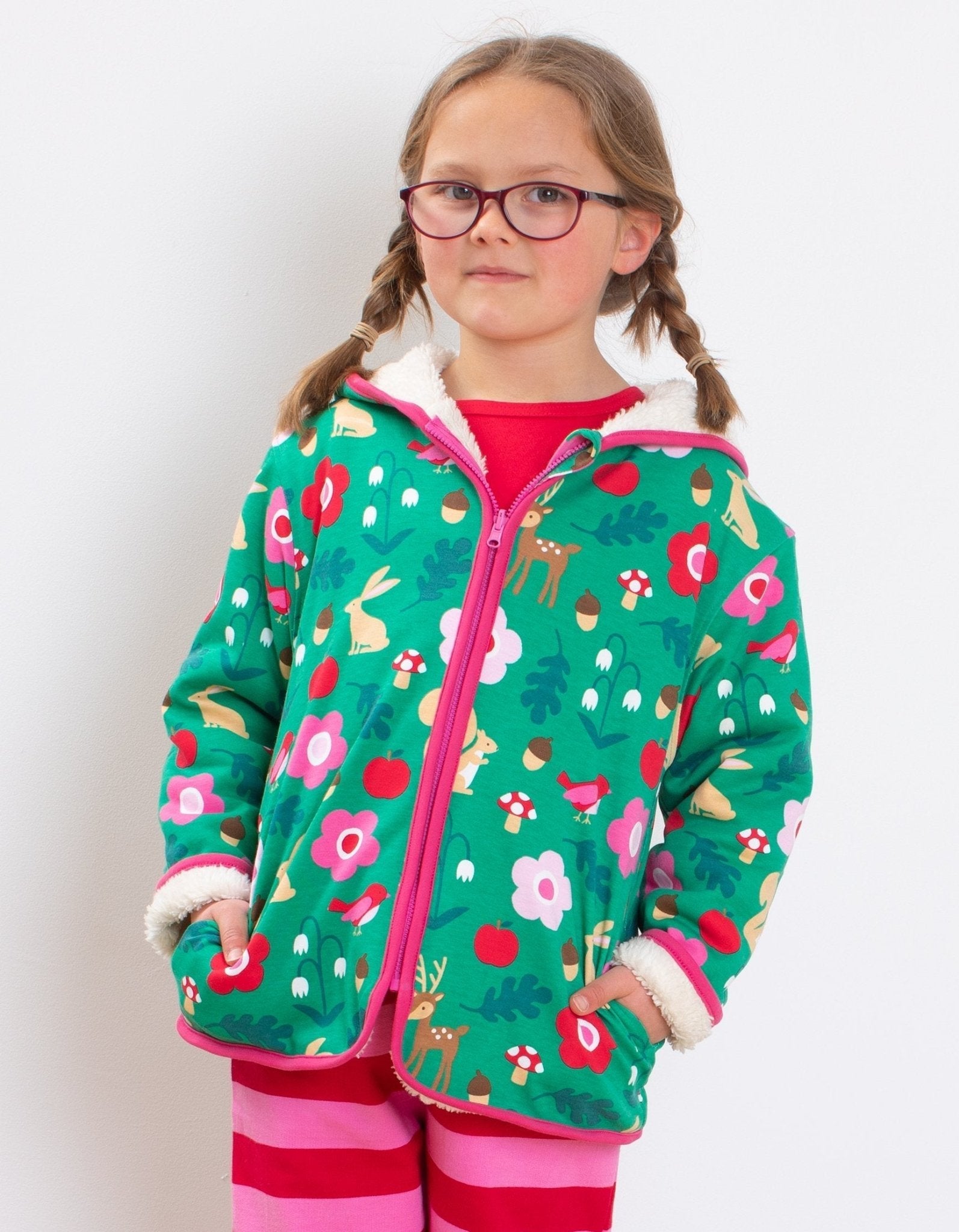 Young girl wearing a green floral-patterned jacket with pink trim on a white background
