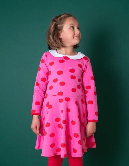 Young girl wearing a pink dress with red apple pattern against a green background