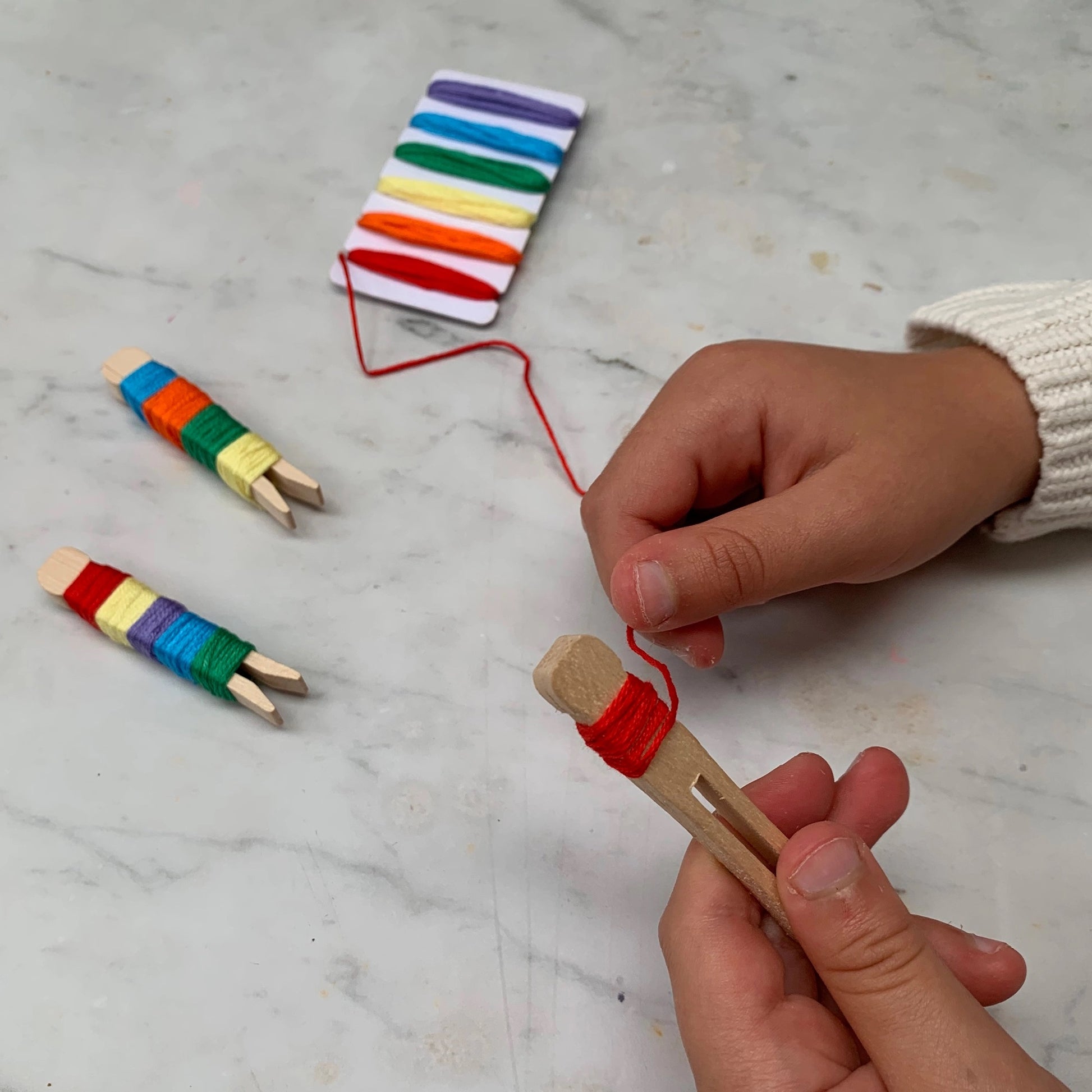 Child's hands working with colorful wooden clothespins and string on a marble surface.