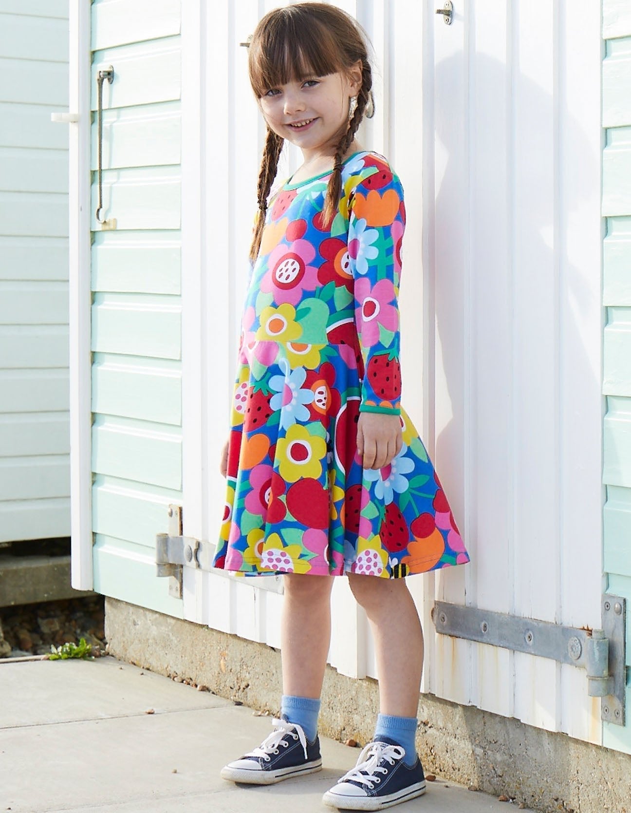 Young girl wearing a colorful floral dress standing in front of a white wooden door.