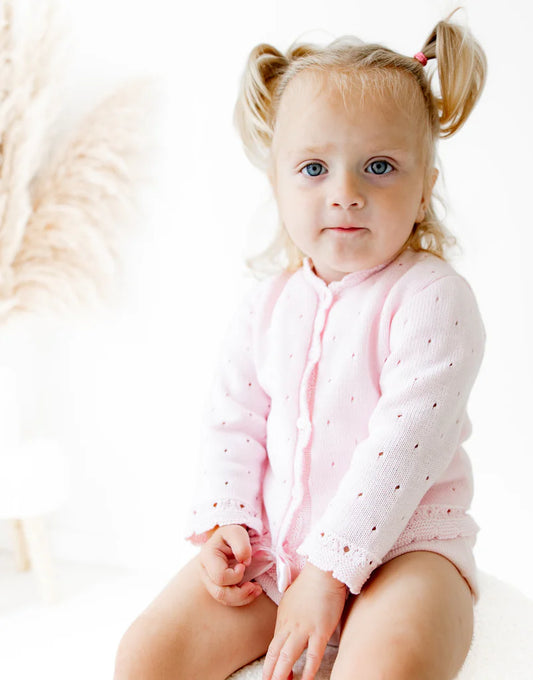 Young child wearing a pink cardigan with a white background
