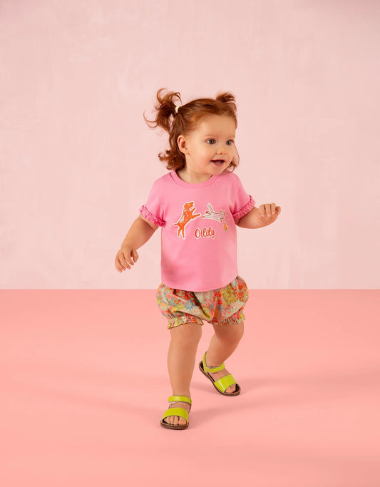Child wearing a pink oilily tshirt with cartoon animals and colorful shorts on a pink background