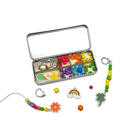 Colorful jewelry-making kit with beads and charms in a metal tin on a white background