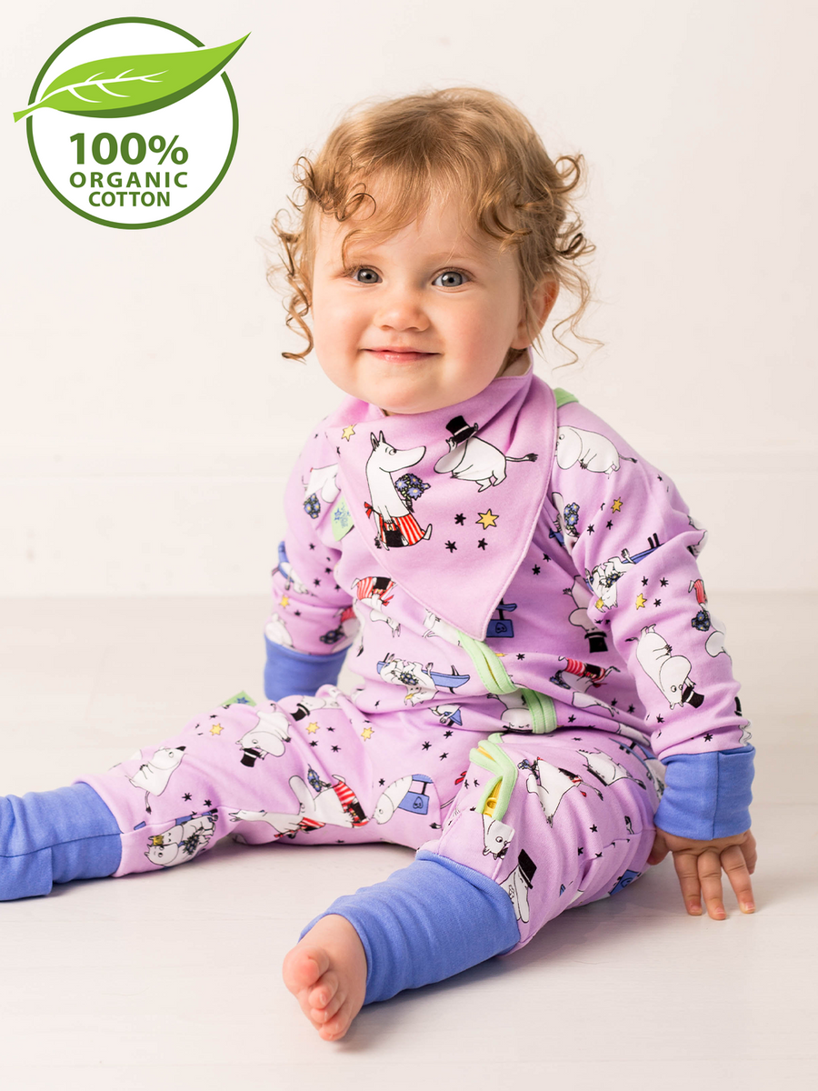 Child wearing a purple outfit with Moomin cartoon characters, sitting on a white background with a green organic cotton label.