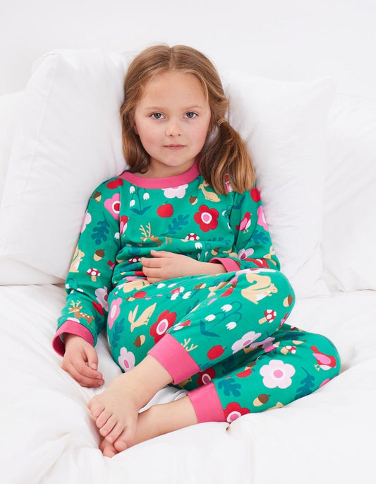 Young girl wearing a colorful floral forest adventure print pyjama set on a white bed.