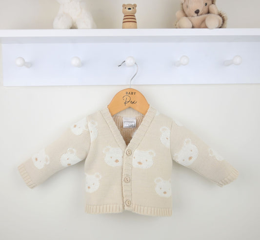 Beige bear face patterned cardigan hanging on a white wooden shelf.