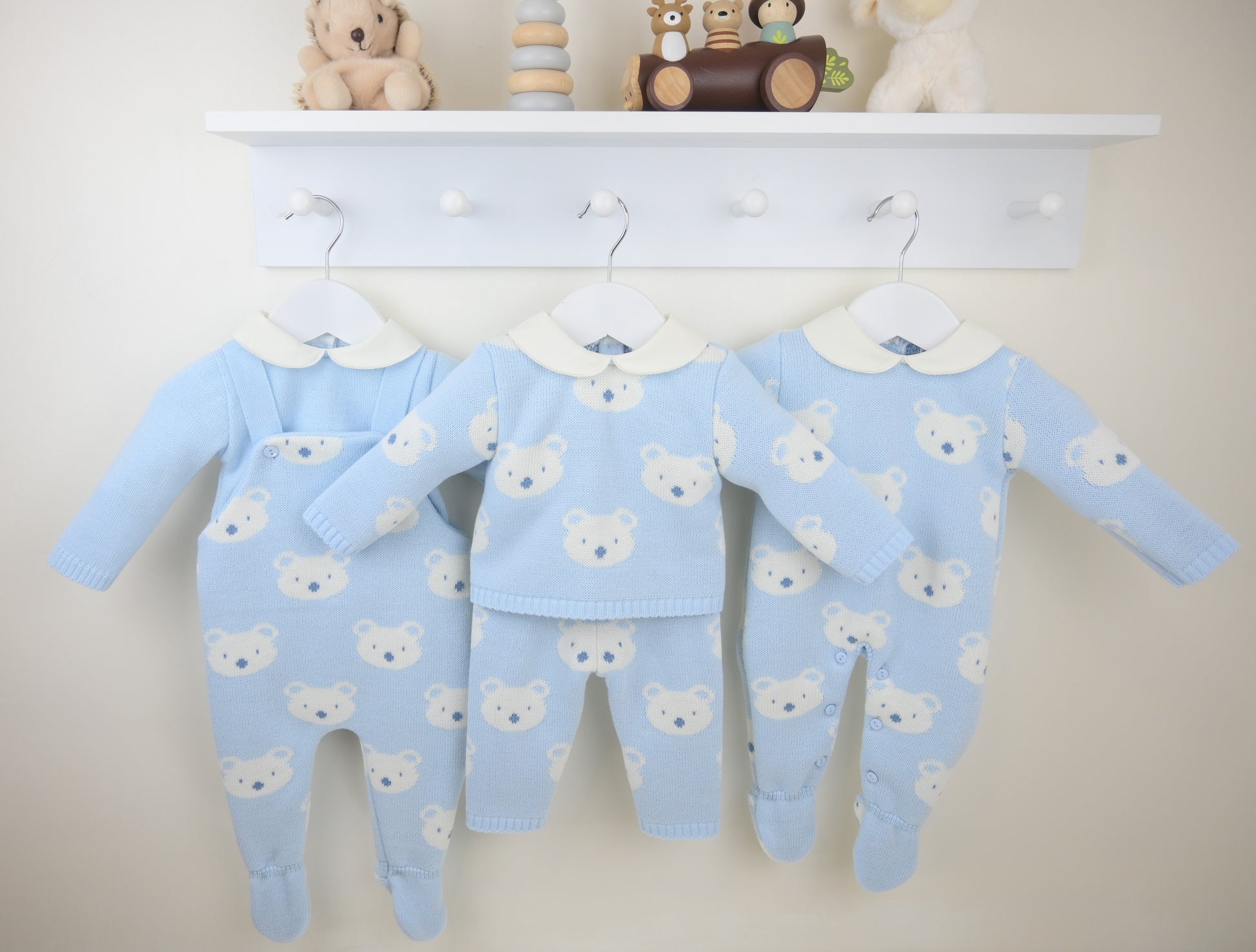 Set of blue baby outfits with bear patterns hanging on a white coat rack.