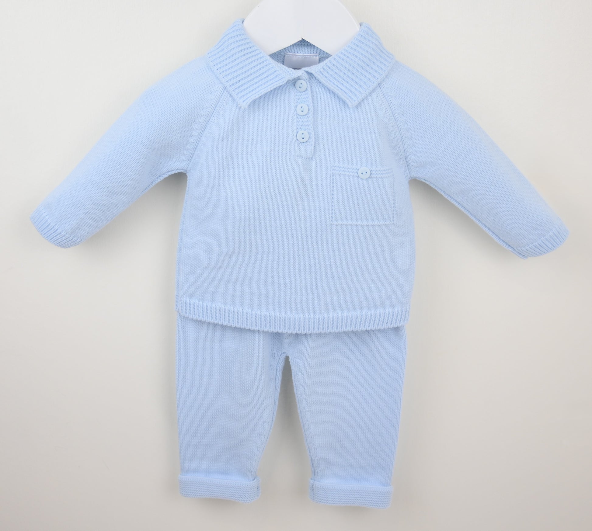 Light blue knitted baby outfit with a shirt and pants on a beige background