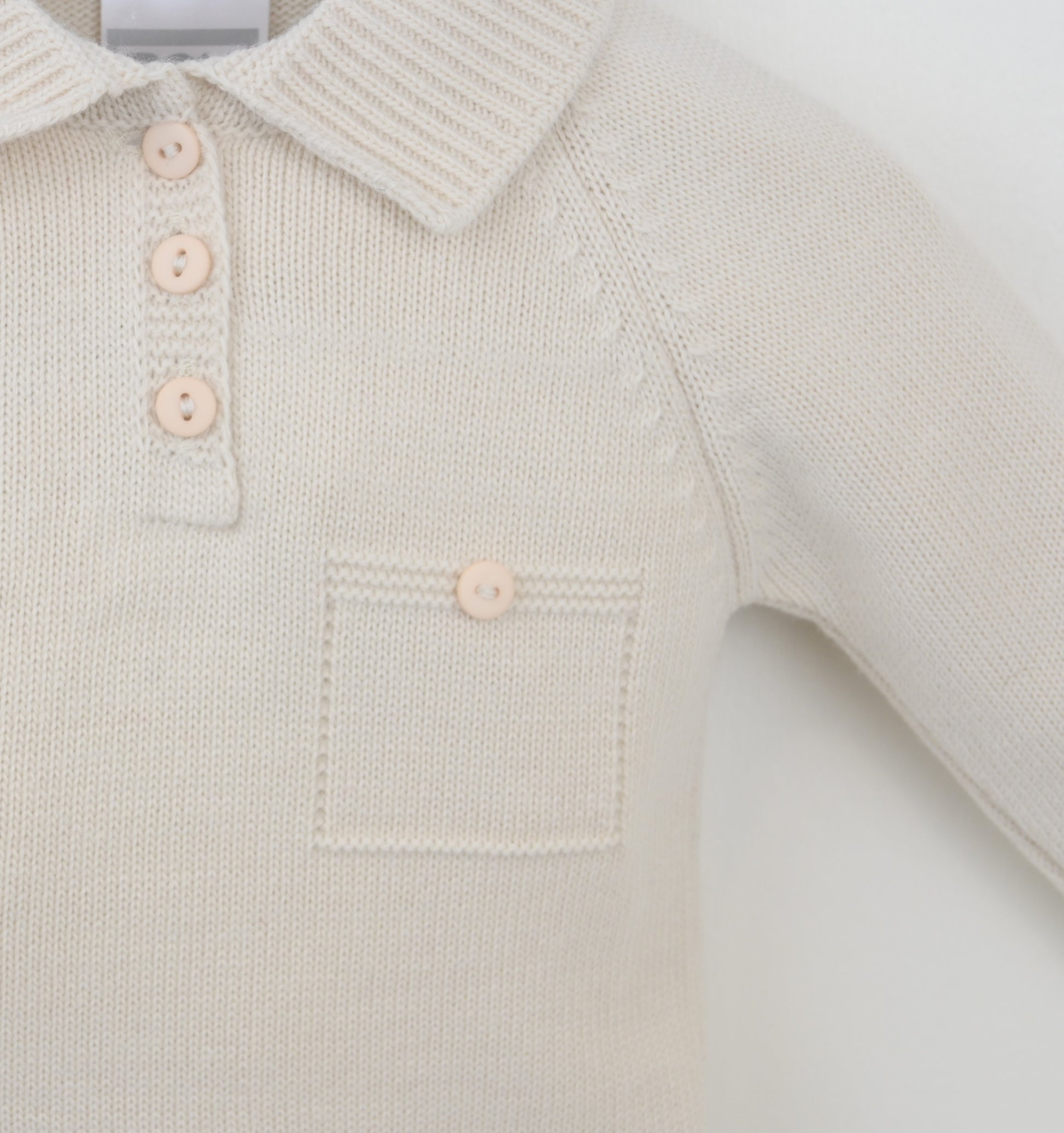 Close-up of a light-colored knitted baby outfit with buttons on a white background
