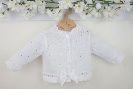 White baby cardigan with a bow on a light background with floral decorations.