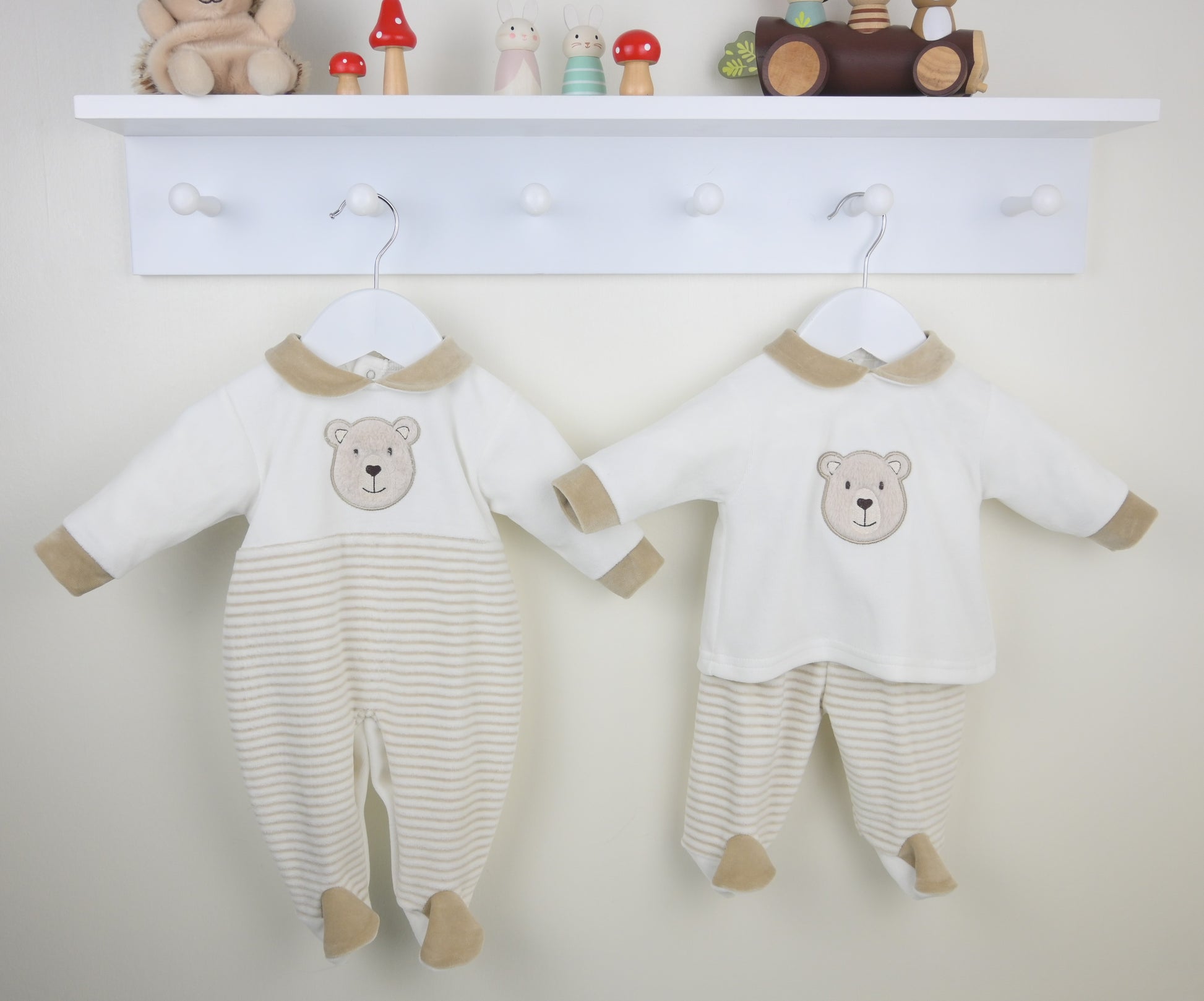 Two baby rompers with bear designs hanging on a white wall.
