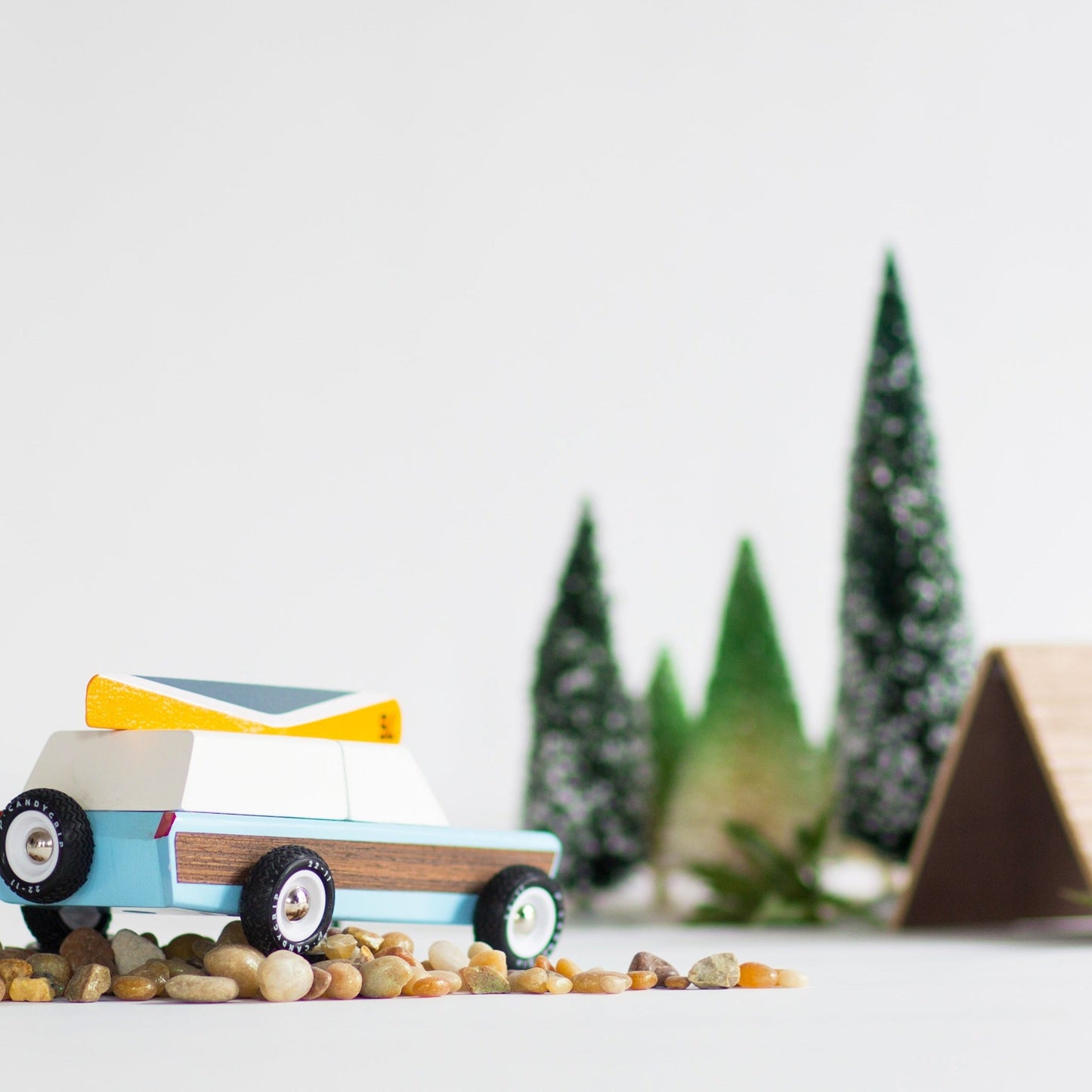 Toy car on pebbles with blurred trees and house in the background