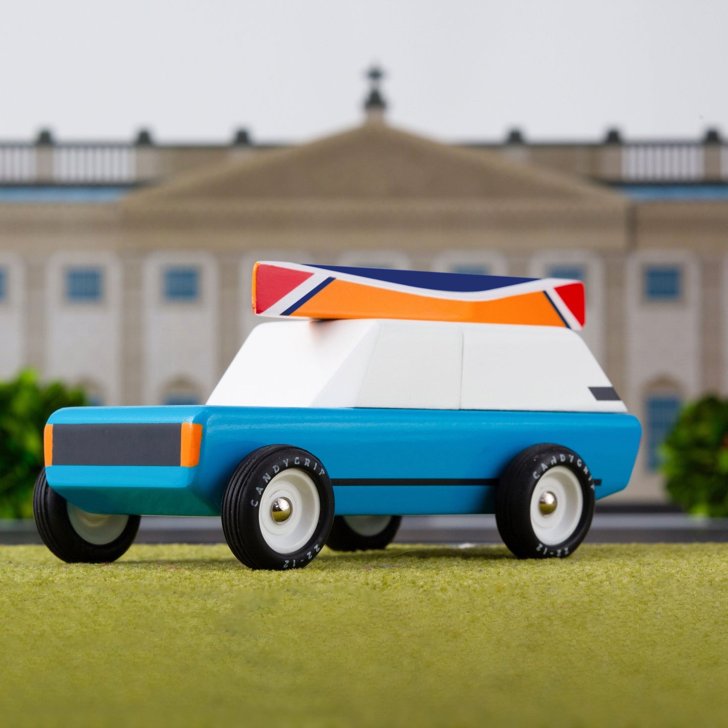 Toy car with a colourful design on a grassy area with a building in the background