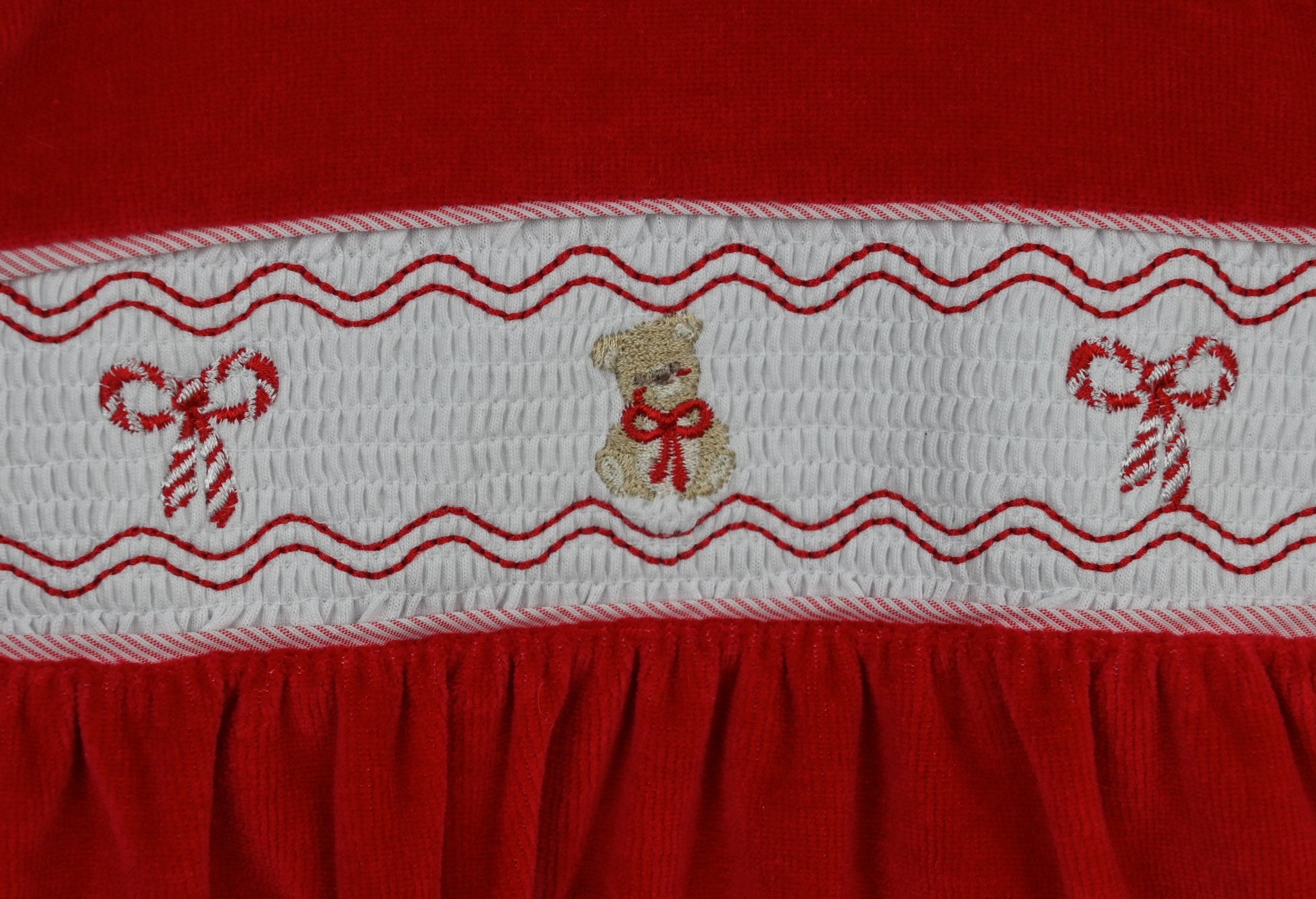 Red fabric with white embroidered border featuring teddy bears and candy canes.