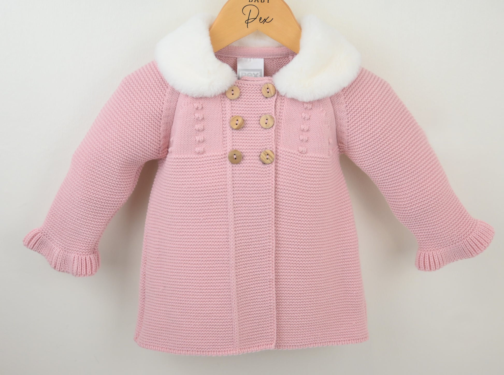 Pink knitted coat with white fur collar on a hanger against a light background