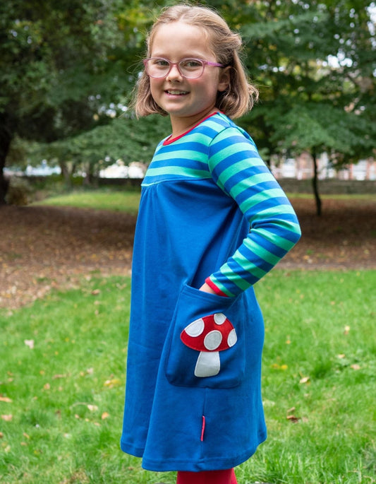 Girl wearing a blue dress with a red and white mushroom design in a park setting