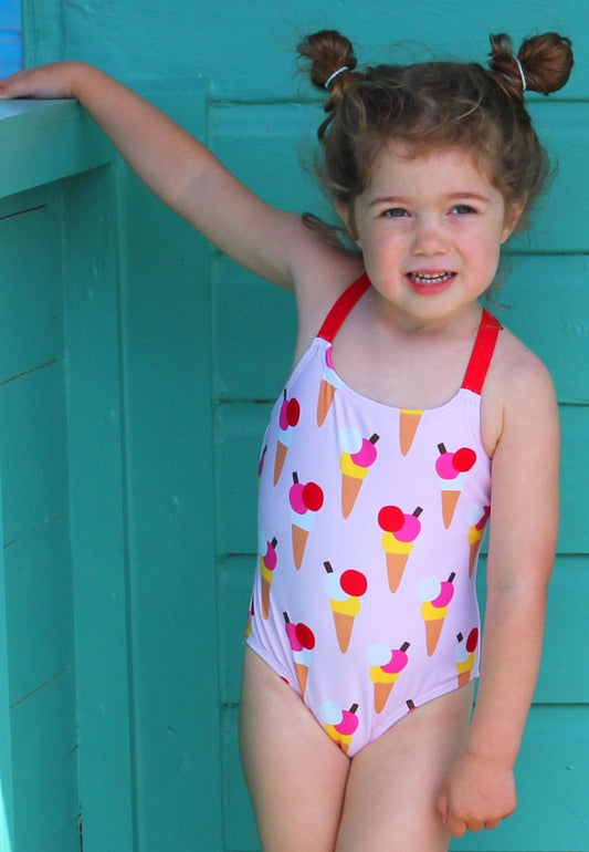 Young girl wearing a colorful swimsuit with ice cream cone pattern against a teal background