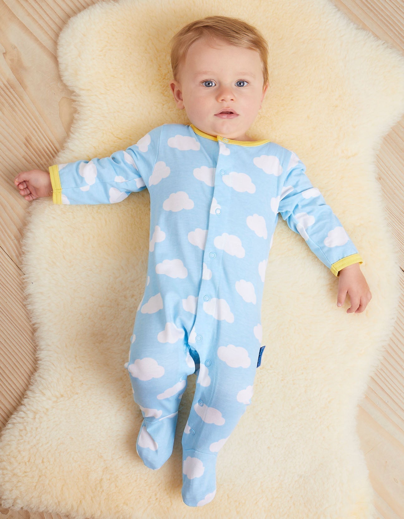 Baby wearing an organic blue babygrow with cloud patterns on a fluffy beige surface.