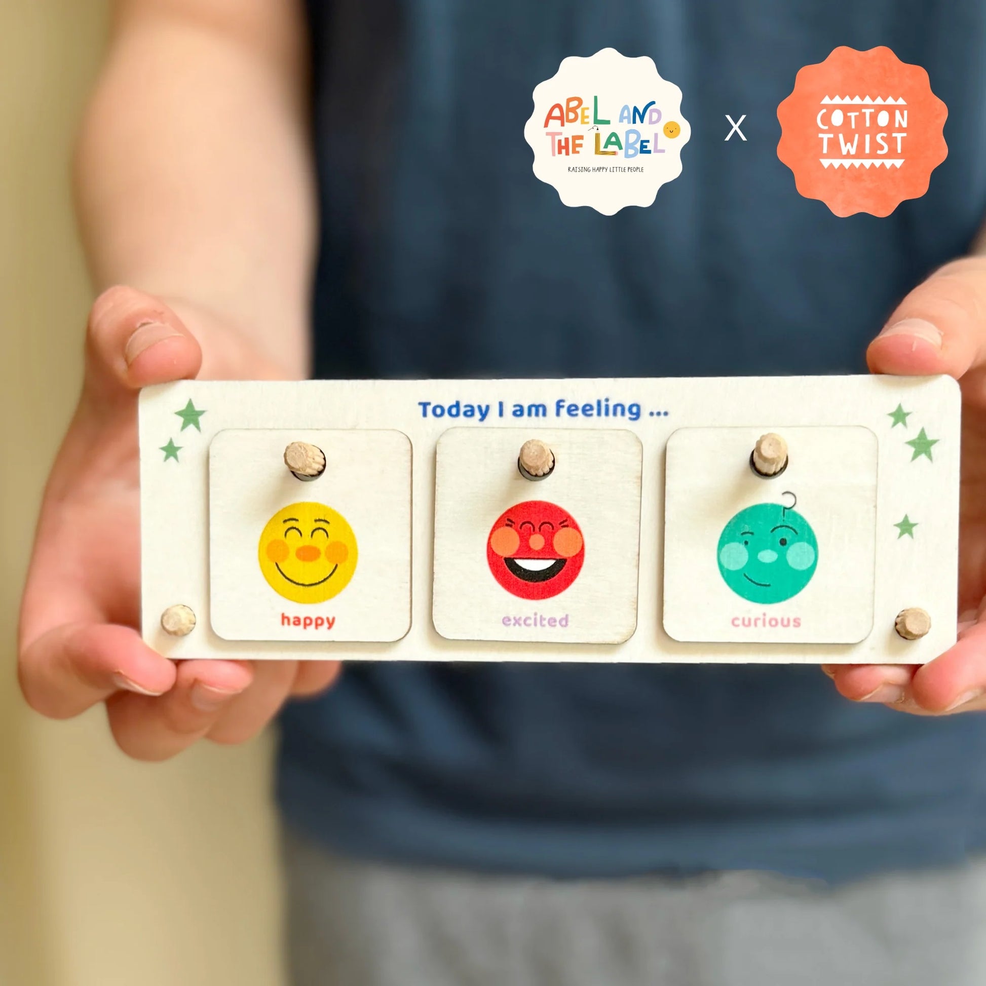 Children's emotional expression card with smiley faces and text held by a person, featuring 'Abel and the label' and 'Cotton Twist' logos.