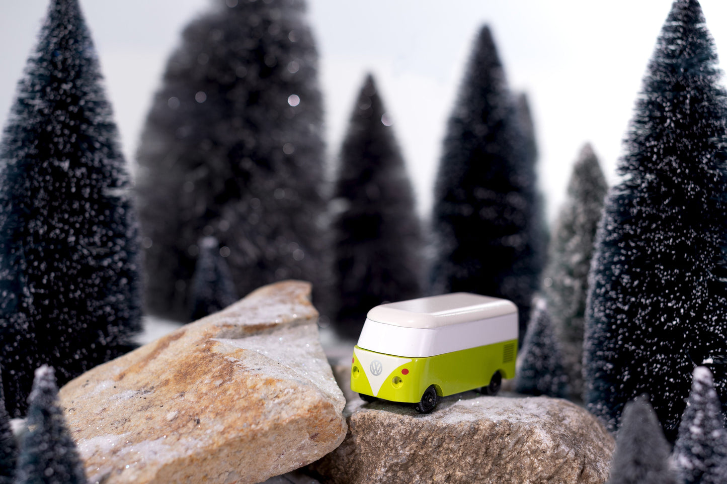 Small green and white toy van on a rock with snowy trees in the background