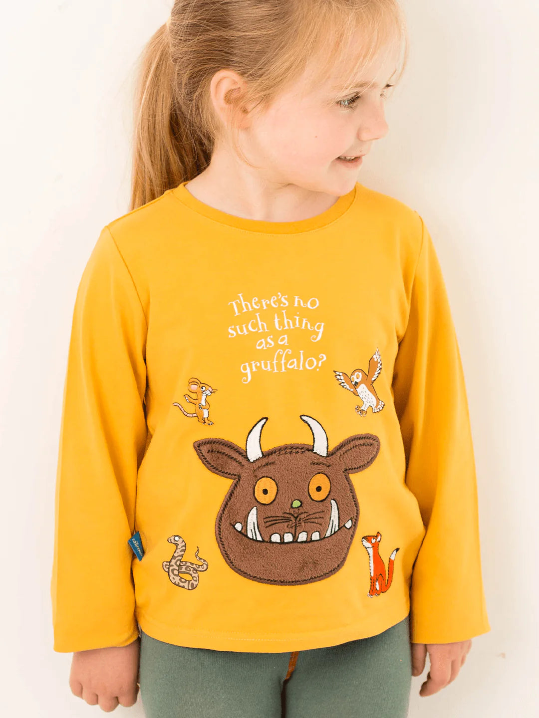 Child wearing a yellow long-sleeve shirt with a gruffalo character design on a plain background