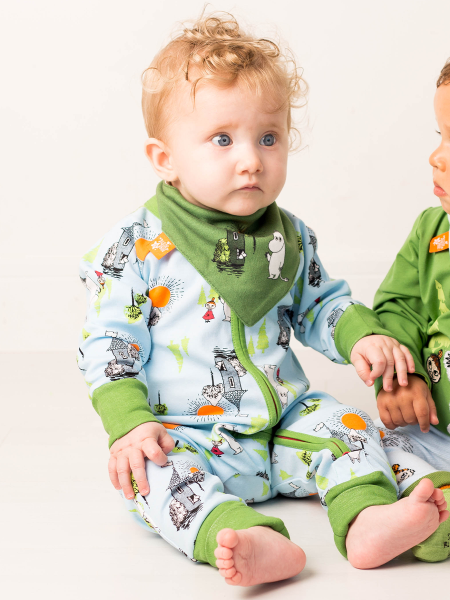Two babies wearing green and blue pajamas with moomin cartoon patterns on a white background