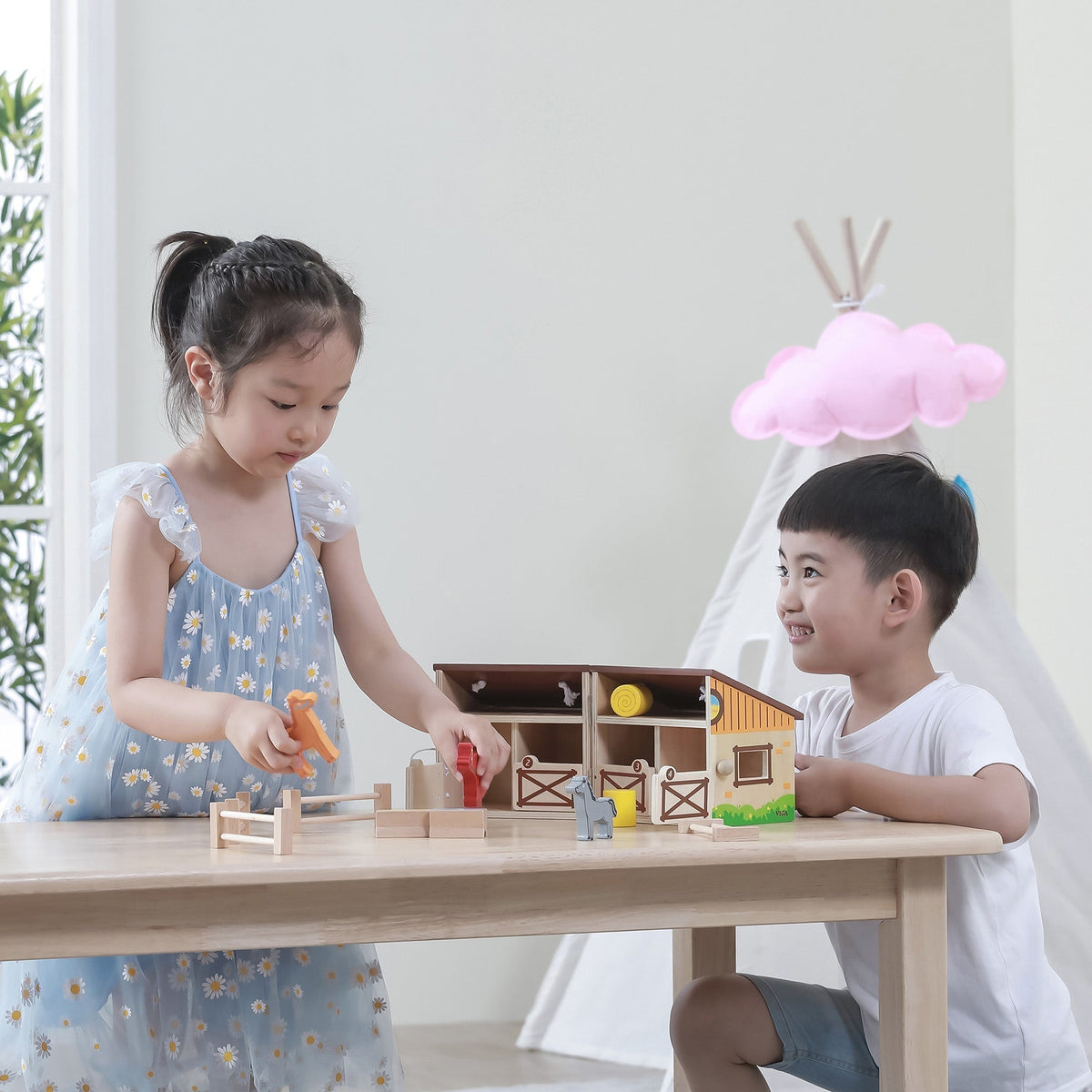 Two children sharing and playing cooperatively with a large open foldable wooden toy stable.
